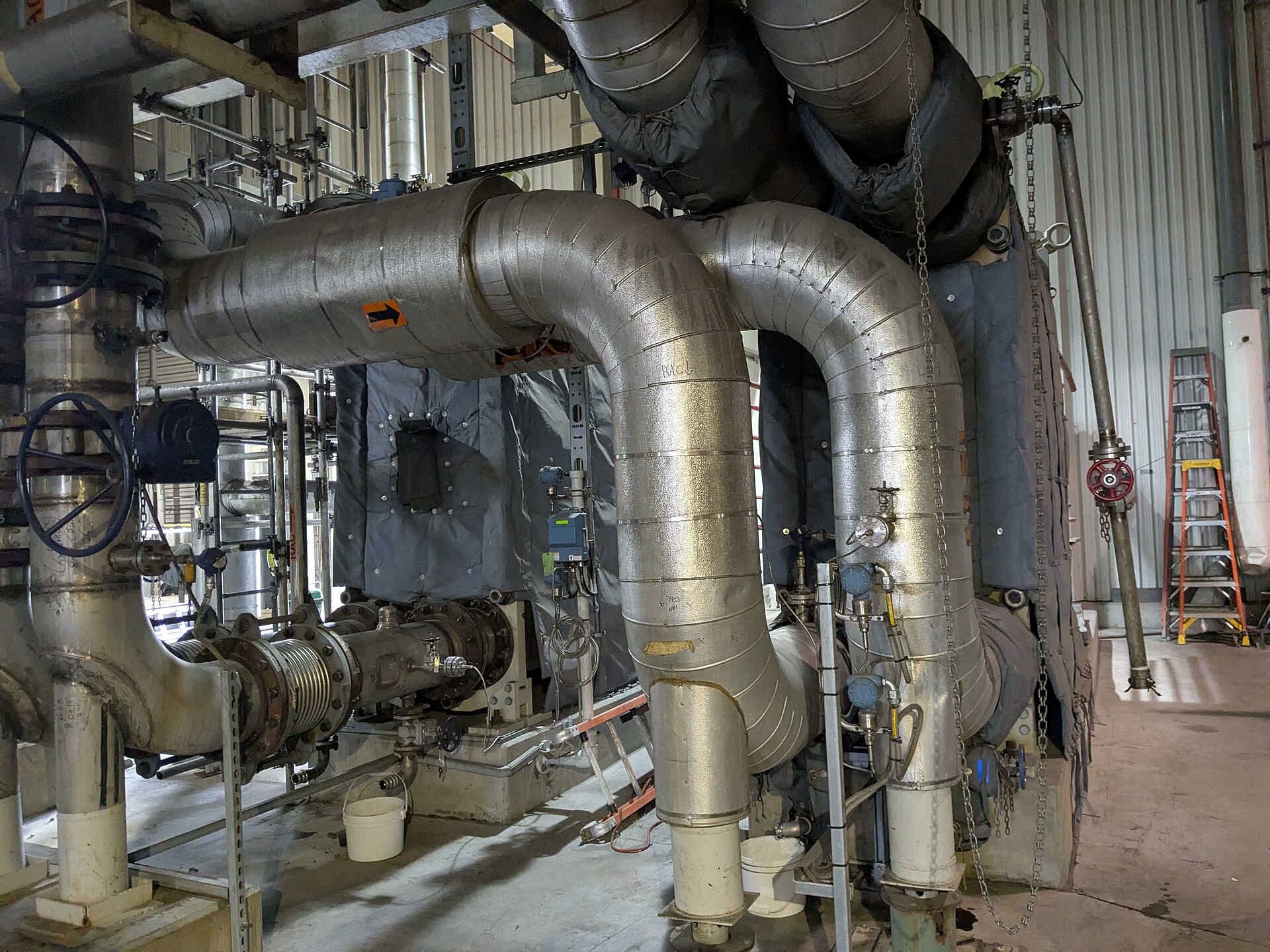An insulated heat exchanger with large piping bends, valves and pressure instruments inside a process plant