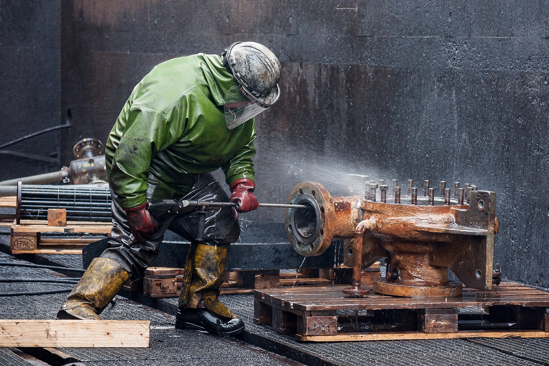 A worker in protective clothing cleaning an industrial surface with a high-pressure jet