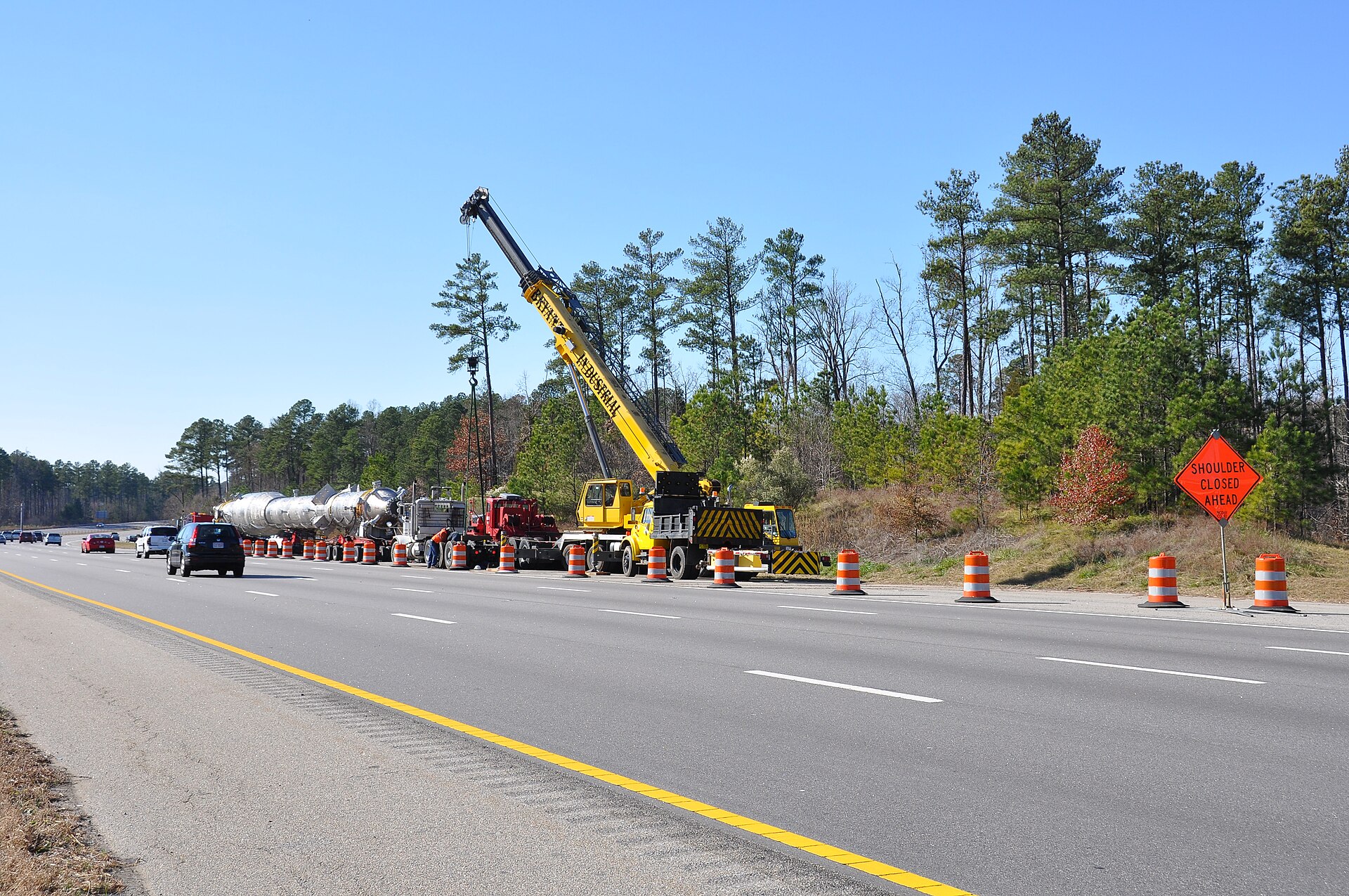A large reactor vessel strapped to a flatbed truck stopped on a highway
