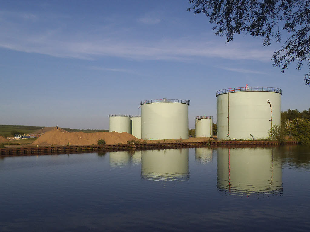 An oil storage tank beside a lane, with a pipe running along its base