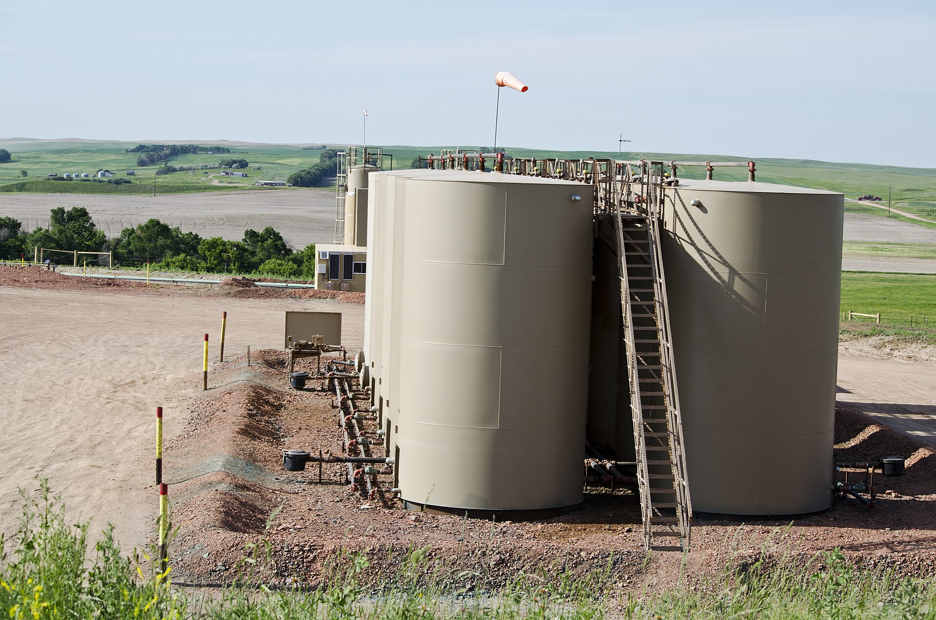 Two oil storage tanks on a fenced pad in open prairie