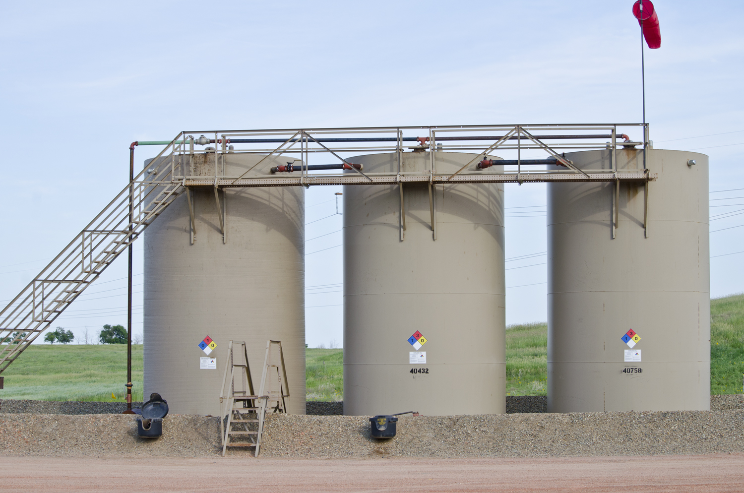 Rows of oil storage tanks with access ladders and pipework at a field site