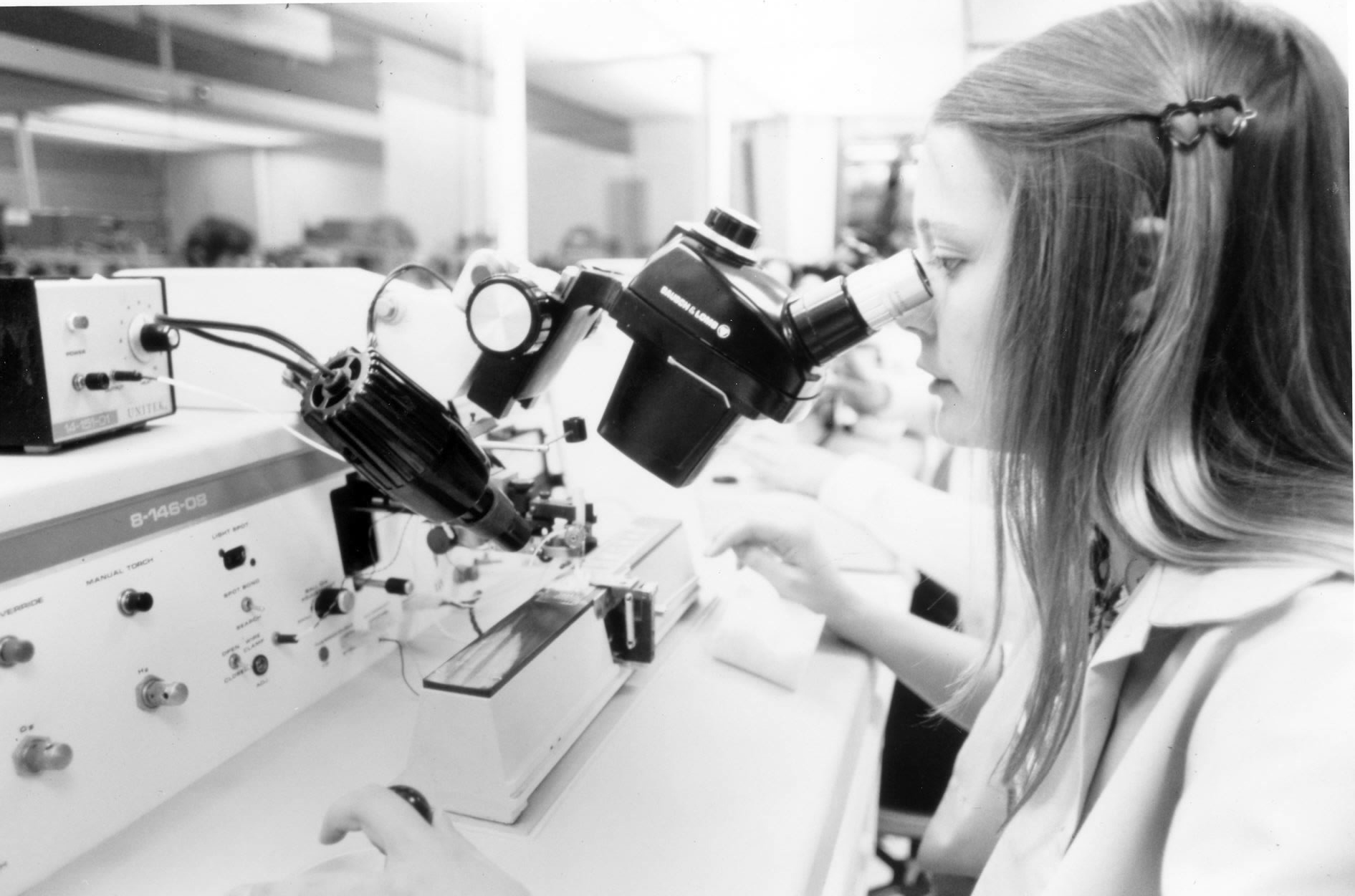 A quality inspector at an electronics plant looking through a stereo microscope at a bonding station