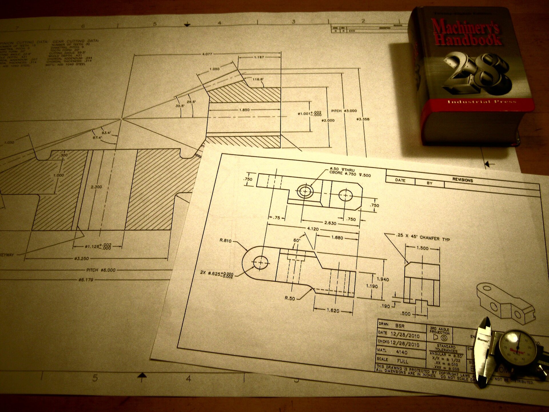 Engineering drawings laid out beside a copy of Machinery's Handbook
