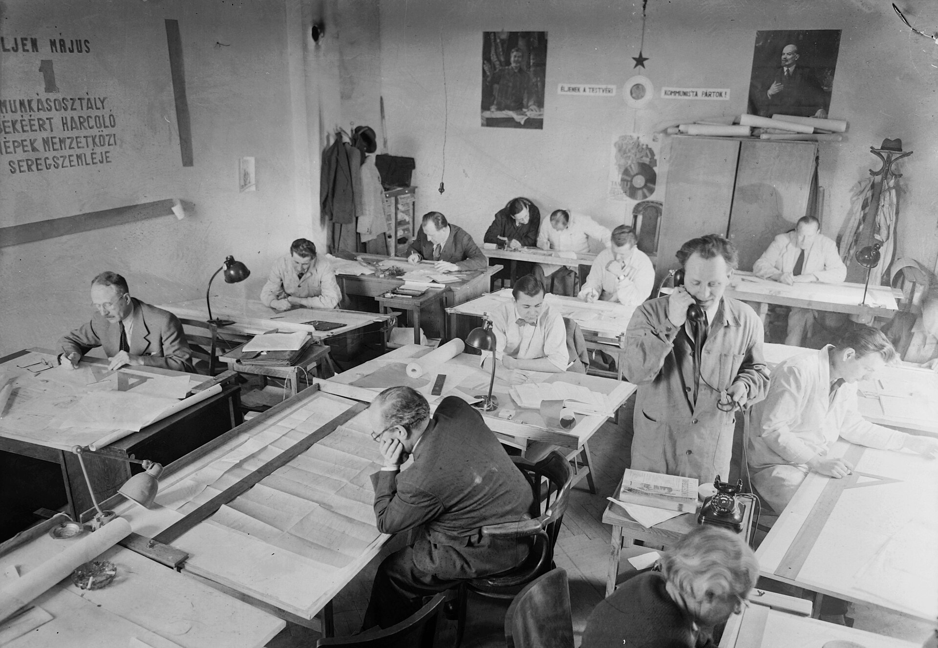 A black and white photograph of a designer at a drawing board with a telephone