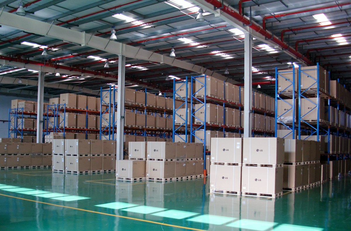 Inside a logistics warehouse: tall racking stacked with palletised goods along a wide aisle