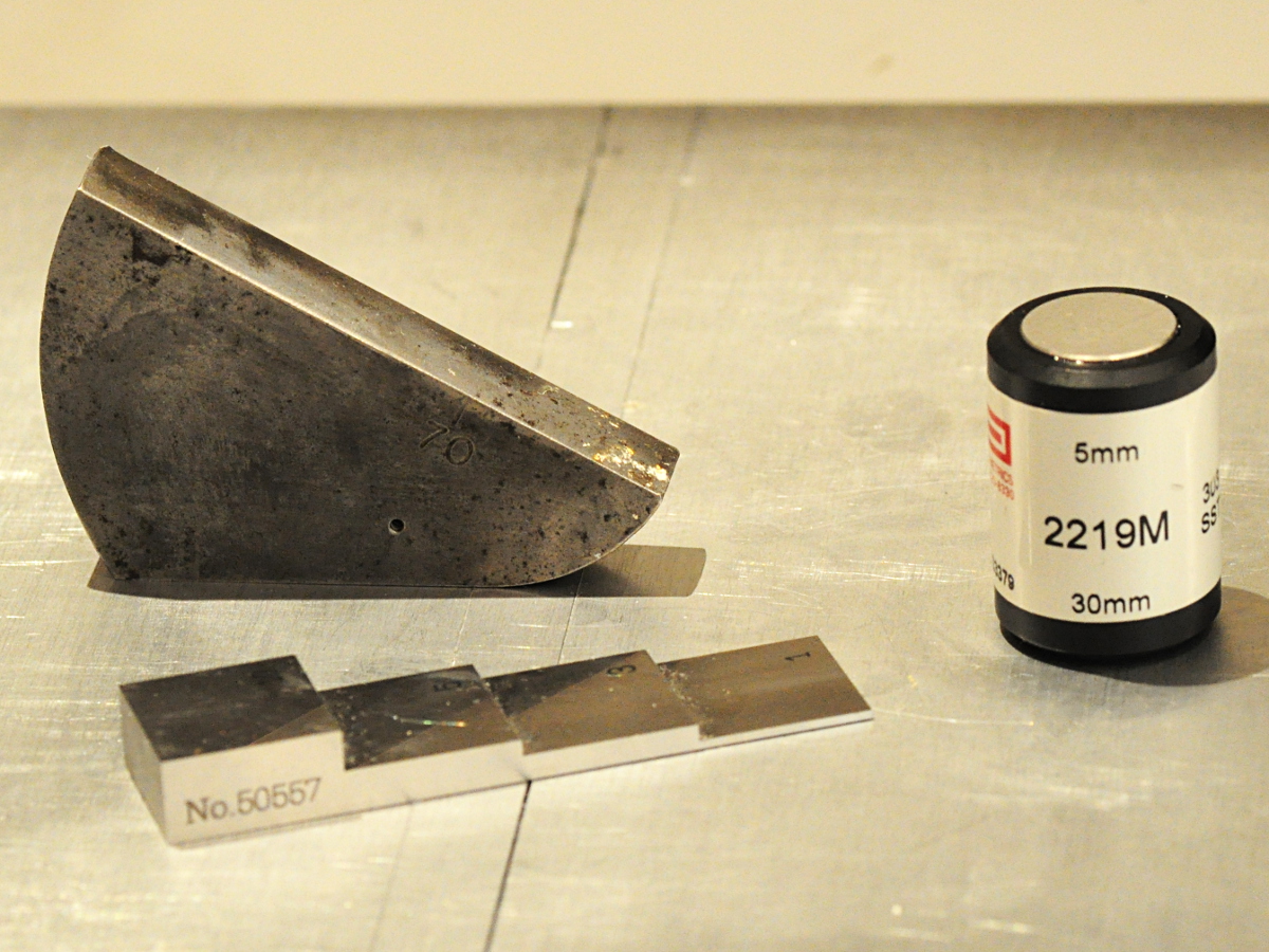 Ultrasonic calibration blocks, a curved angle beam block and a step wedge, next to a 5 mm ultrasonic probe